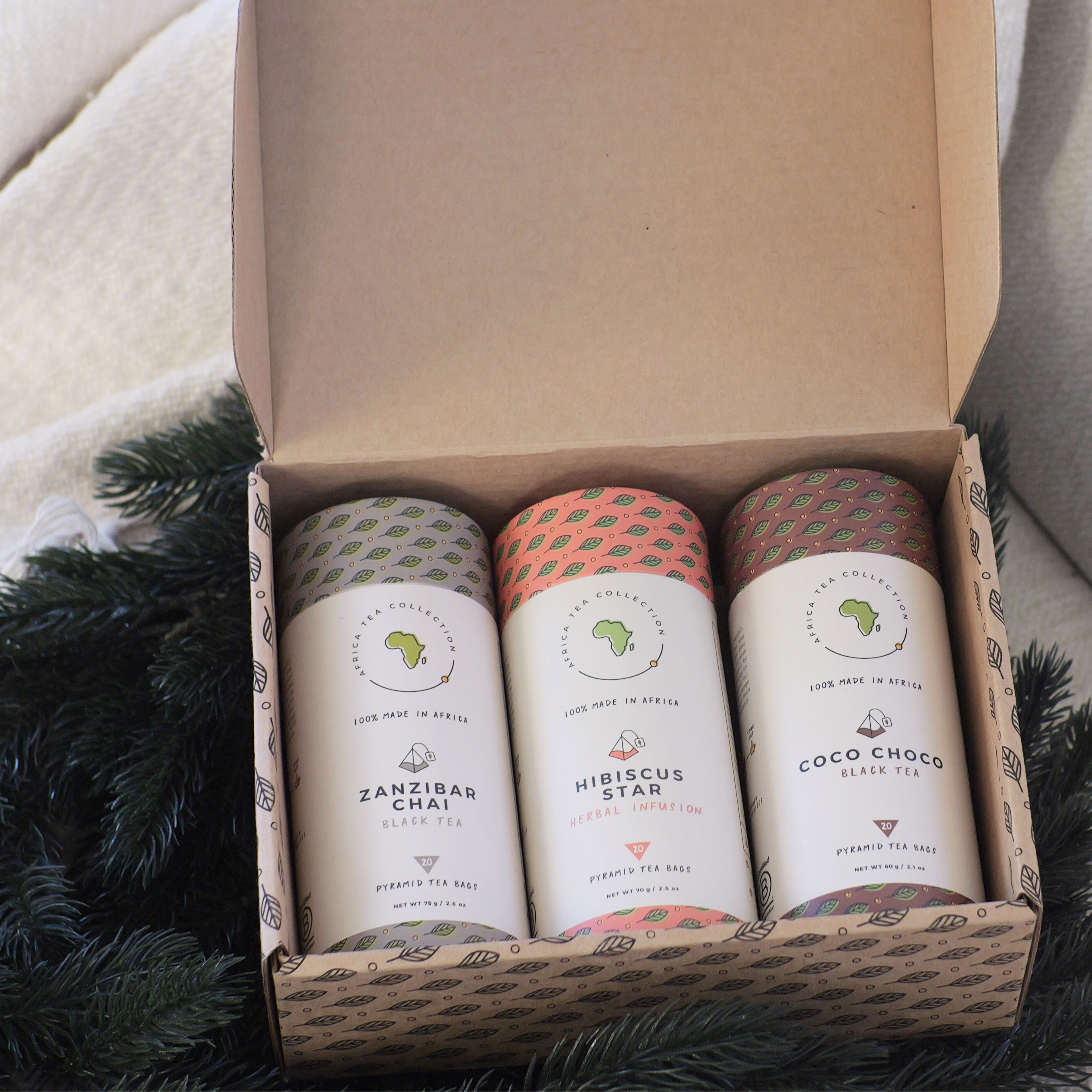 Three tea blends in a cardboard box with decorative paper, surrounded by greenery.